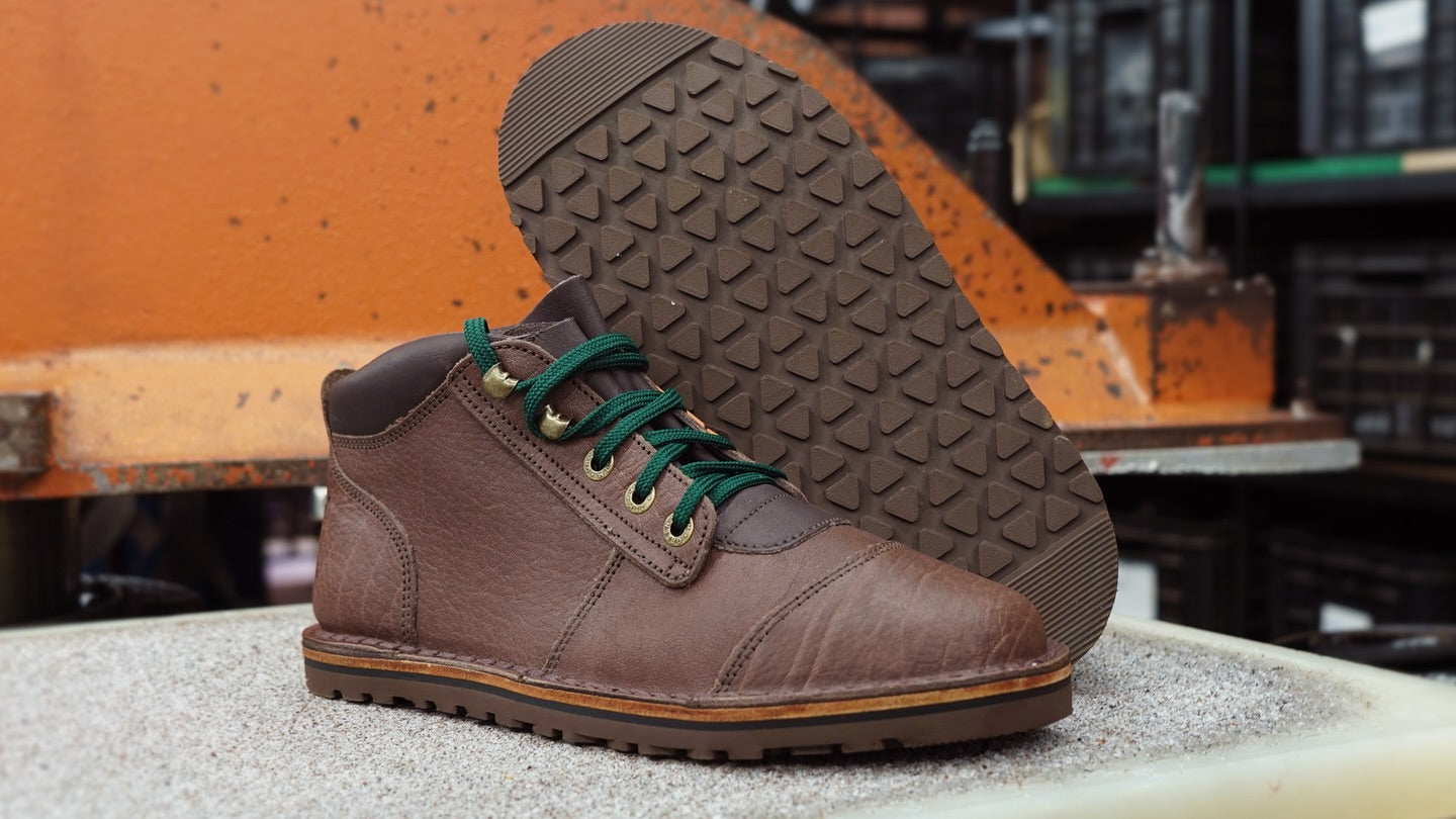 Brown leather shoe with green laces on a concrete surface with a blurred industrial background
