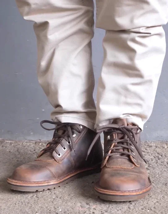 Brown leather boots worn with beige pants on a gray background