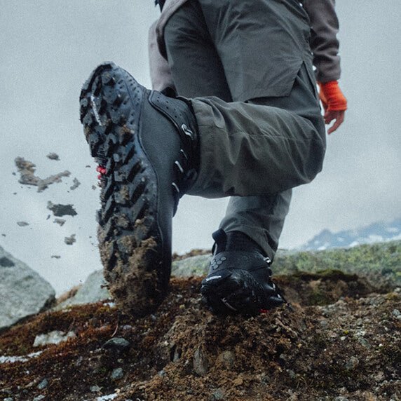 Person wearing hiking boots on a rocky trail with a mountainous background