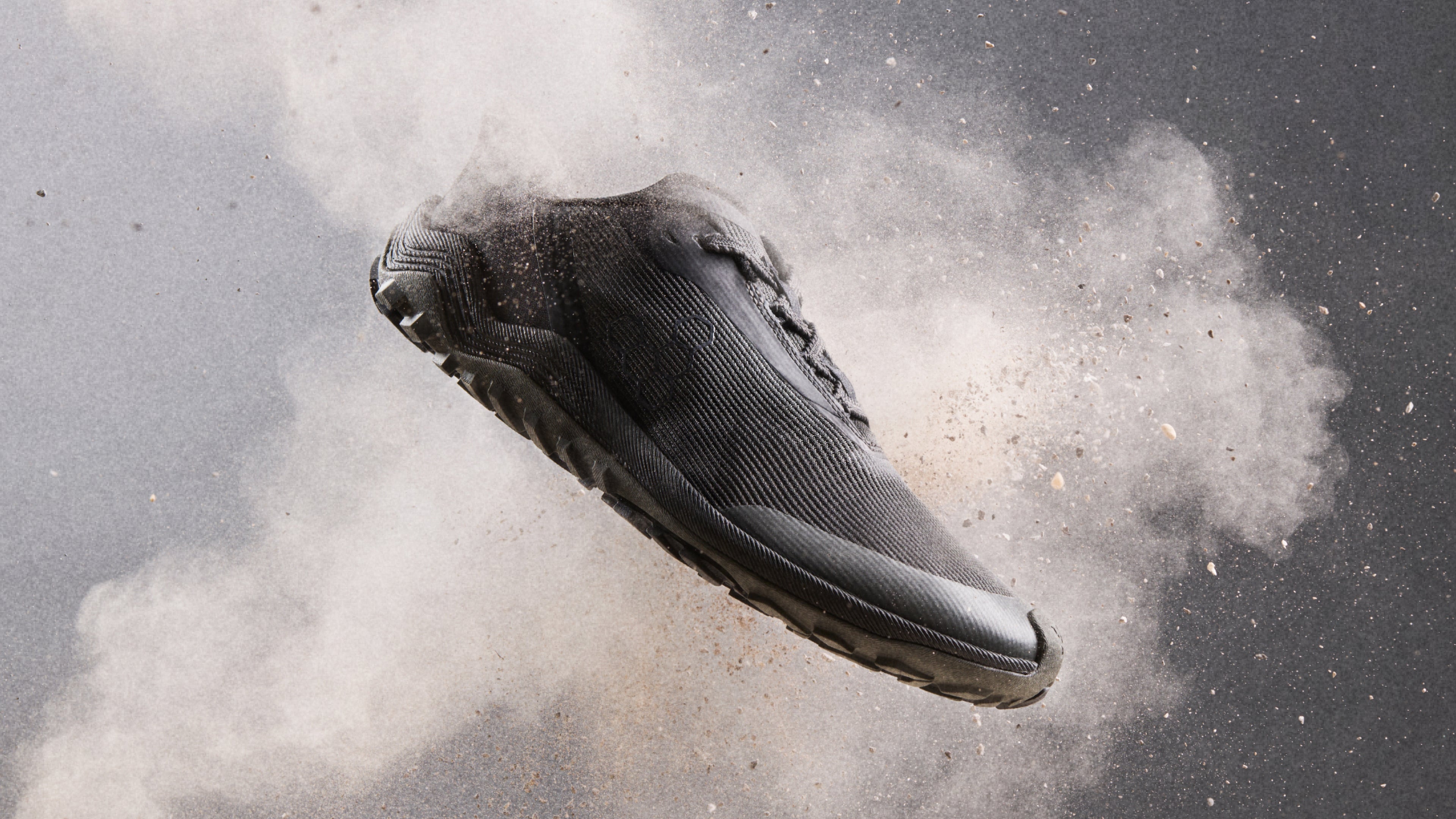 Black sneaker in mid-air with a cloud of dust on a dark background