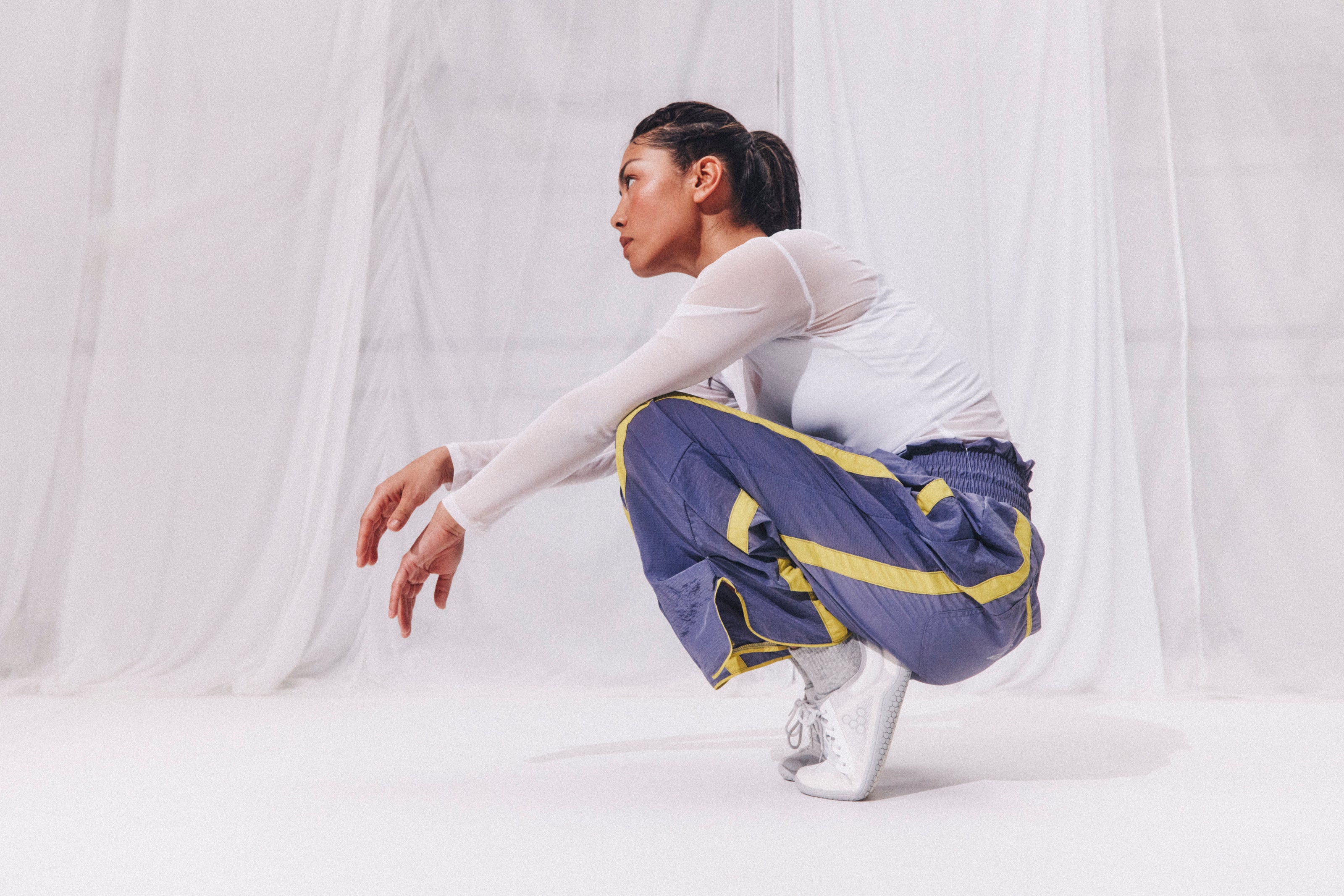 Person wearing a white long-sleeve top and blue pants with yellow accents, sitting on a white floor.