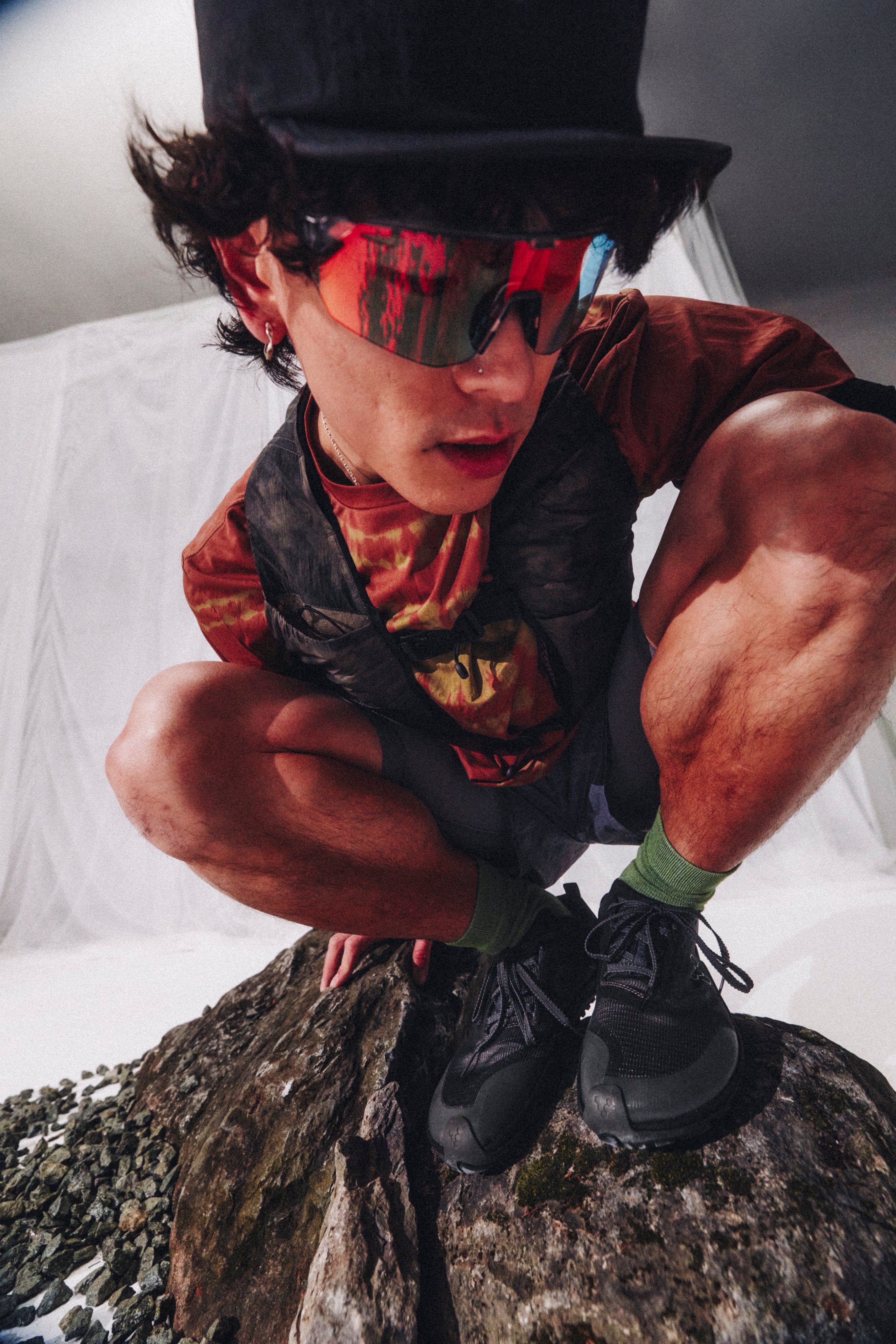 Person wearing a top hat and sunglasses crouching on a rock