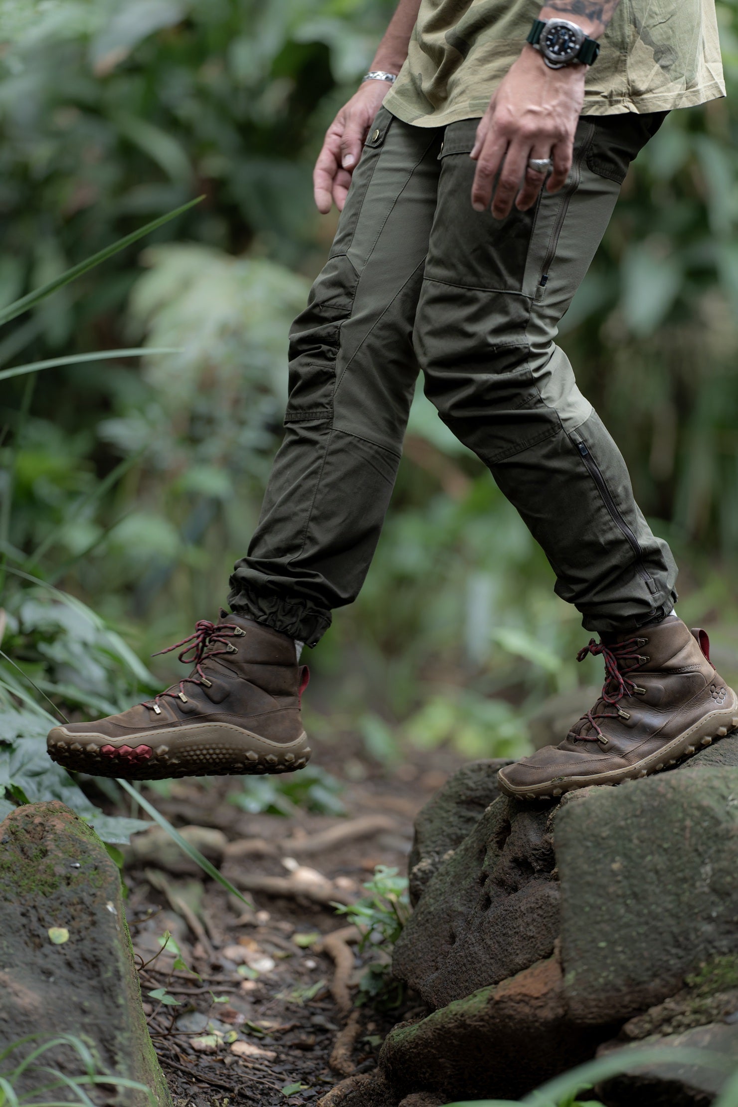 Person wearing green pants and brown boots walking on a rocky path in a forest.